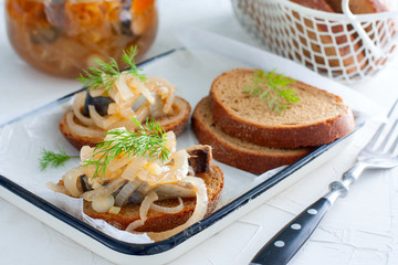 Marinated herring and onion on rye bread on white table, horizontal
