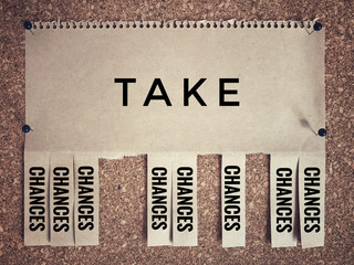 Motivational and inspirational quote - ‘Take chances’ on a white paper and sticked on a bulletin board. With vintage styled background.