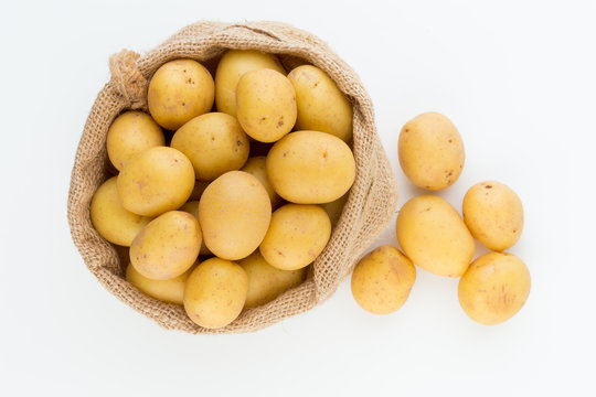 Sack of fresh raw potatoes on wooden background, top view