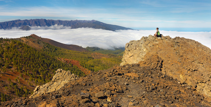 Man sitting on the rock watching a volcanic landscape with a Caldera de Taburiente on background, island of La Palma, Canary Islands, Spain