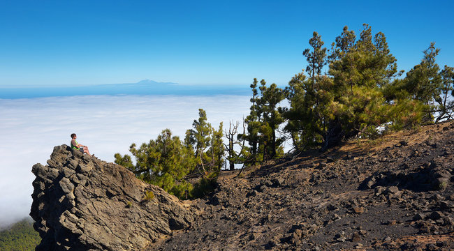 Man sitting on the rock watching a volcanic landscape with a mountain of Pico de la Teide on background, island of La Palma, Canary Islands, Spain