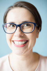 Beautiful woman in elegant glasses smiling and looking up while standing on light blue background. 