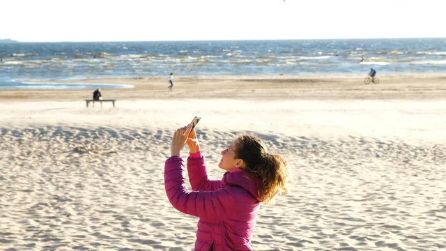 Girl tourists taking pictures on your smartphone of seagulls and kite surfers on the sea