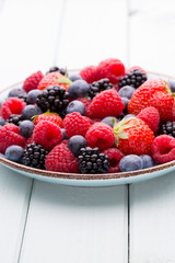 Fresh berry salad on blue dishes. Vintage wooden background.