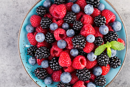 Fresh berry salad on blue dishes. Vintage wooden background.