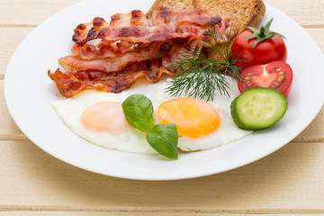 Fried eggs with bacon on the wooden table.