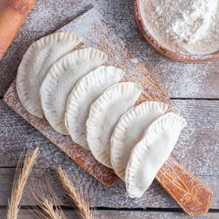 Raw chebureks on a wooden board, top view, selective focus