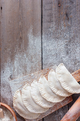 Raw chebureks with meat, prepared for frying on a wooden board with flour, top view, copying space