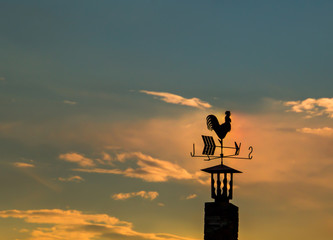 Iron rooster weather-vane showing a wind direction. Traditional weathercock on sunset heaven background.