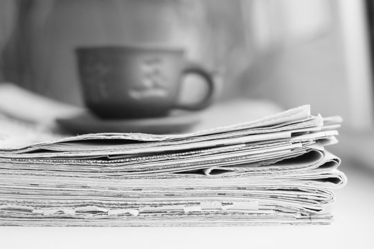 Stack of newspapers and cup of tea. Concept for business morning, reading fresh daily papers with news and having a breakfast. Journals and ceramic mug, selective focus on pages     