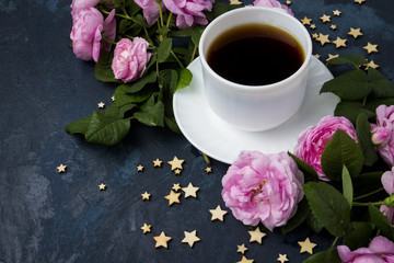White cup with black coffee, stars and pink roses on a dark blue background. Concept of coffee with flowers and the night sky