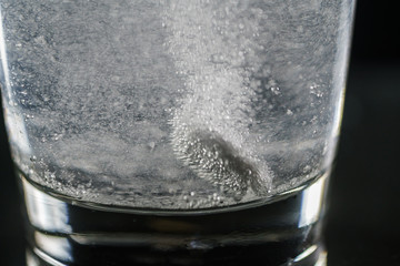 Glass with efervescent tablet in water with bubbles isolated on white