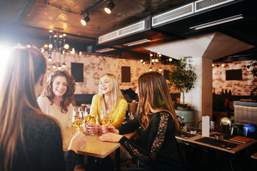 Female friends drinking wine and chatting while sitting in the bar.