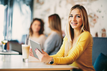 Fototapeta premium Young caucasian woman using tablet while sitting in cafe and drinking coffee.
