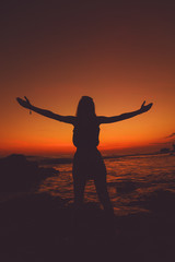 Fototapeta premium Girl with arms wide open enjoying sea / ocean scenery in sunset.