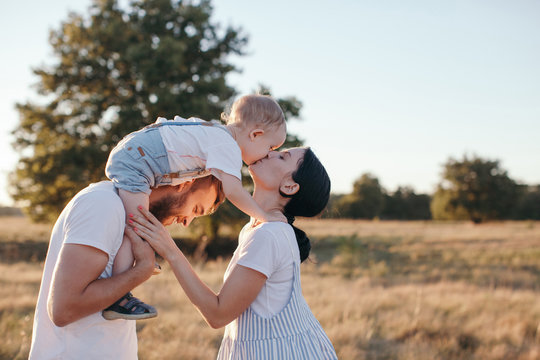 Unusual family portrait with son sitting on shoulders of his father and kissing his mom