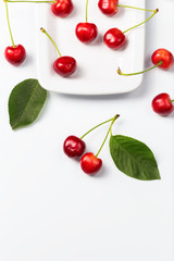 Obraz na płótnie Canvas Cherry berries and cherry leaves on white plate.Food frame. Space for text.