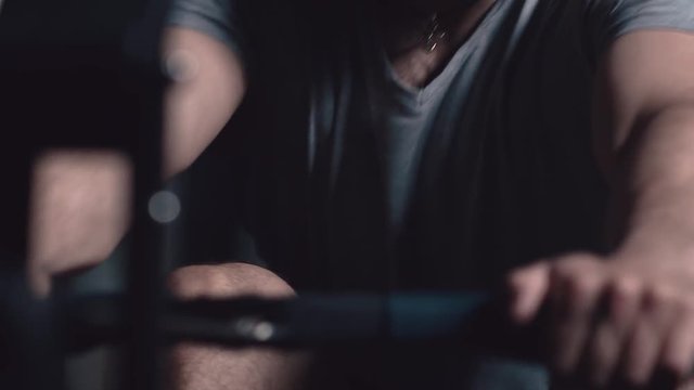 Sport in slowmotion. Men's hands hold the handle of the rowing machine: it pulls the handle with power, makes a jerk. Training on the simulating rowing. Development of strength and muscles. Close-up
