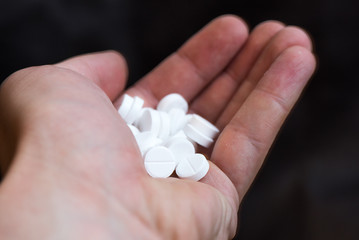 White pills in hand on black background closeup