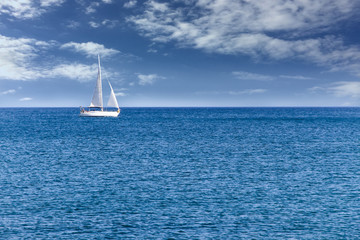 Fototapeta premium White modern yacht sailboat sailing alone on calm blue sea waters on a beautiful sunny day with blue sky and white clouds.