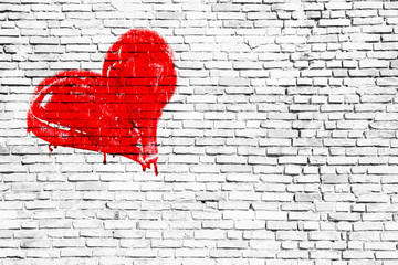 Red colored heart manually painted with drips and dry paint imperfections over a simple grungy white brick wall texture background. Symbolic for love, romance, passion, couple, valentines.