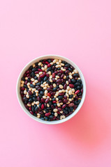 Mix of raw beans in a white bowl on a pink background. Top view and copy space.