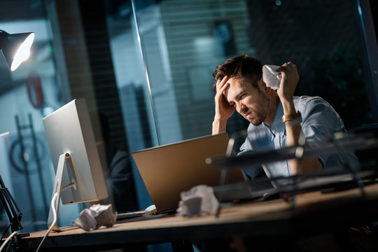 Casual man having problems at work and crumpling papers being uninspired and watching at laptop