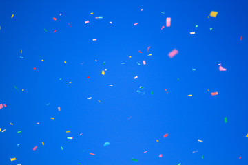 multicolored confetti on clear blue sky background. Concept of holiday backdrop