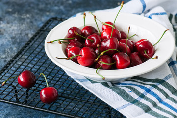 Naklejka na ściany i meble Fresh ripe red cherries in a white plate on a wire rack. Close up. Organic food concept.