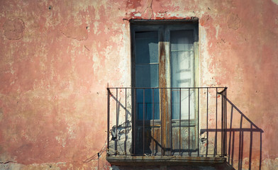 Fototapeta na wymiar Rustic old grungy and weathered wooden closed door of rusty balcony with a red brown vintage cracked wall with peeling paint in a Southern Italy house typical facade.