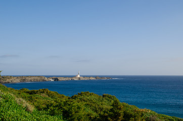Landscape photography of a lighthouse of Menorca by day with rocks and sea.