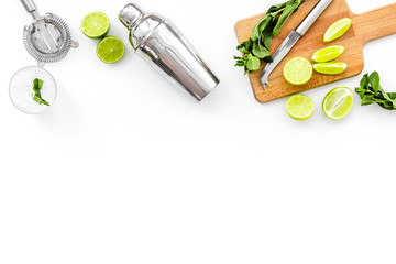 Make mojito cocktail with lime and mint. Shaker, strainer, glass near slices of lime on cutting board on white background top view copy space