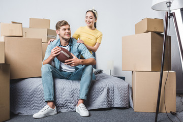 Fototapeta na wymiar beautiful young couple sitting in bedroom of new home with american football ball