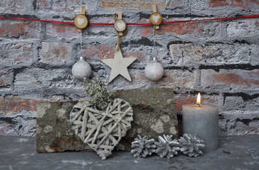 Brennende Kerze und Weihnachtsdekoration vor Ziegelmauer