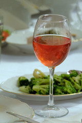 Vertical picture. A glass of pink wine on a table next to a broccoli salad.