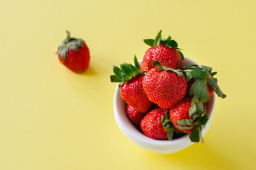 Heap of fresh ripe strawberries in a white bowl on a yellow background. Overhead view and copy space. Organic food concept.