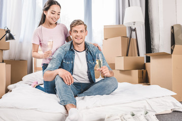 happy young couple sitting on bed with champagne after moving into new home