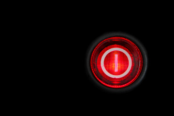 Round red power (on and off) button or switch with retro illumination glowing in the dark macro photography and isolated on a dark black background.