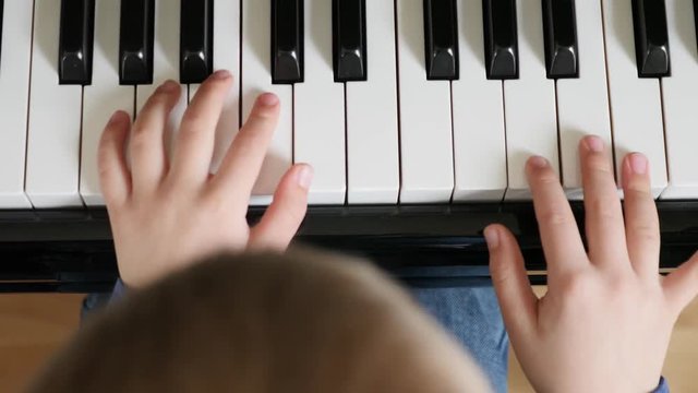 A cute little boy practicing a black upright piano at home