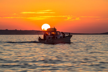 Naklejka na ściany i meble Sunset over sea with silhouette of small boat