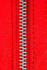 Red zipper tightly closed binding together two layers of fabric textile and red leather under high magnification close detail photography as texture background.