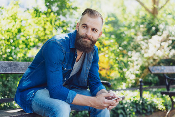 Naklejka na ściany i meble Attractive bearded man siting on a park bench