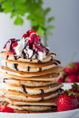 Stack of pancakes with strawberries, whip cream and chocolate syrup on a white plate on a white background. Copy space.