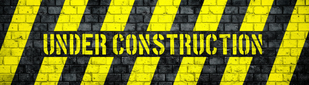 Under construction warning sign with yellow and black stripes on concrete wall texture background in wide panorama format. Concept for do not enter the area, caution, danger, construction site.