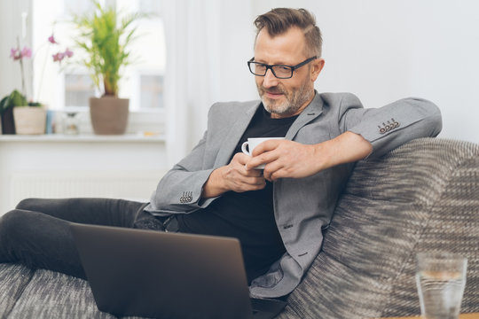 Man using laptop while having coffee on sofa
