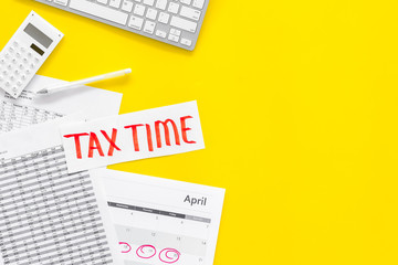 Tax time lettering on office work desk with calendar and bills on yellow background top view copy space