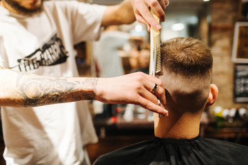 Hairdresser blow drying his client in barbershop. Barber using scissors and comb