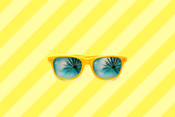 Summer concept image: yellow sunglasses with palm tree reflections isolated in large yellow striped background. Minimalist image ready for summer, sun protection, hot days, tropical travel vacation