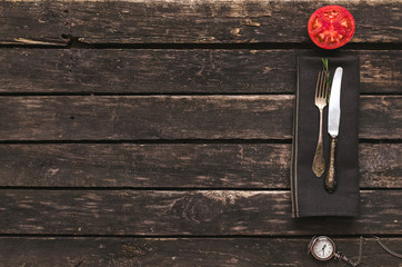 Fork and knife on table cloth towel,sliced red tomato and pocket watch on the kitchen wooden table background with copy space. Dinner time.