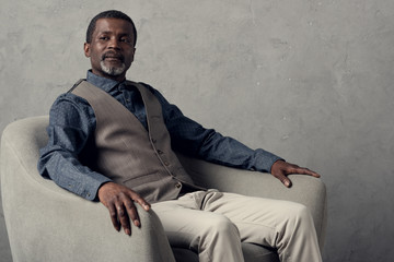 middle agedf serious african american man in waistcoat sitting in armchair